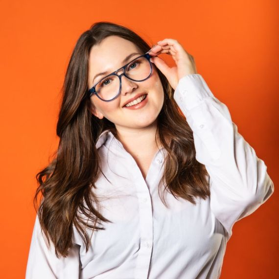 Hymyilevä, silmälasipäinen nainen oranssia taustaa vasten