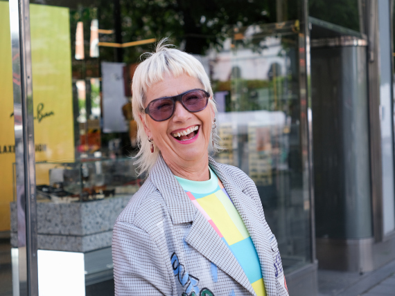 Lena Sjödin skrattar med färgskiftande glas utanför en Synsambutik.